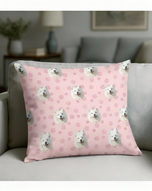 Pink pillow with white dog faces and paw prints on a gray couch.