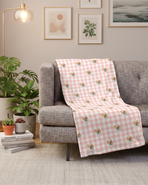 Pink checkered blanket with dog pattern draped over a gray sofa in a living room.