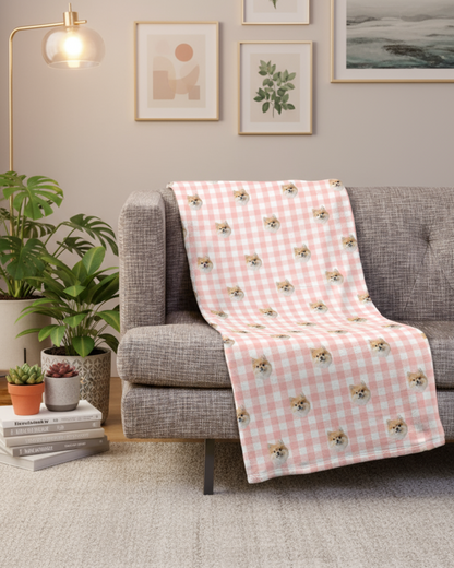 Pink checkered blanket with dog pattern draped over a gray sofa in a living room.