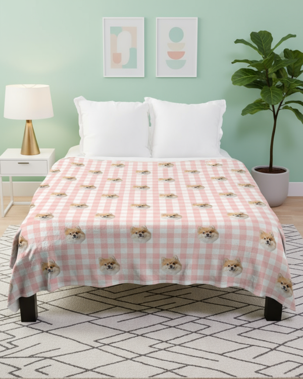Bed with pink checkered blanket featuring dog illustrations in a room with a green wall, nightstand, and plant.