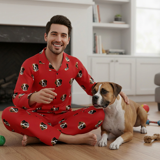 Man in red pajamas with dog pattern sitting on the floor with a dog.