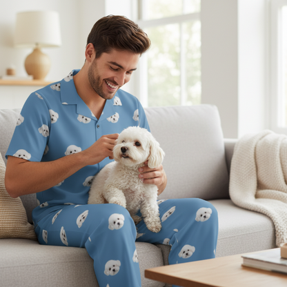 Man in blue pajamas with dog patterns sitting on a couch holding a small white dog.